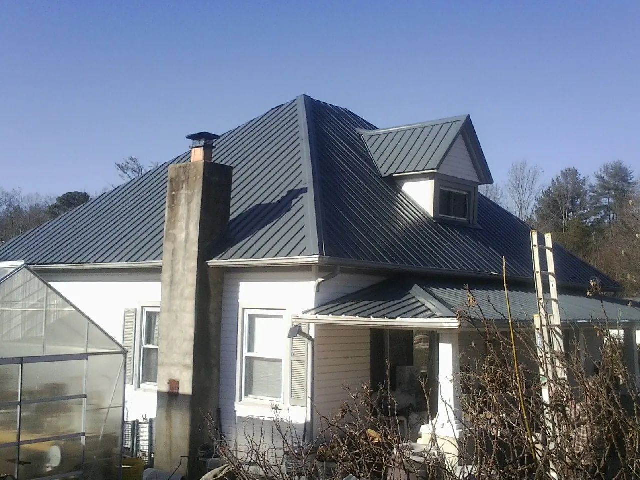 Dark blue standing seam metal roof on a white farmhouse with dormer — Slate & Tile Roof Repair by Roofing Brothers in Cogan Station