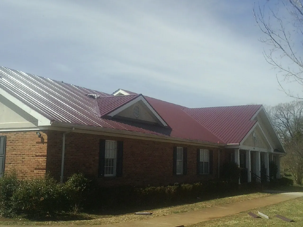 Red metal roof with gabled entries on a long brick building, from a Hail Damage Roof Repair job in Cogan Station