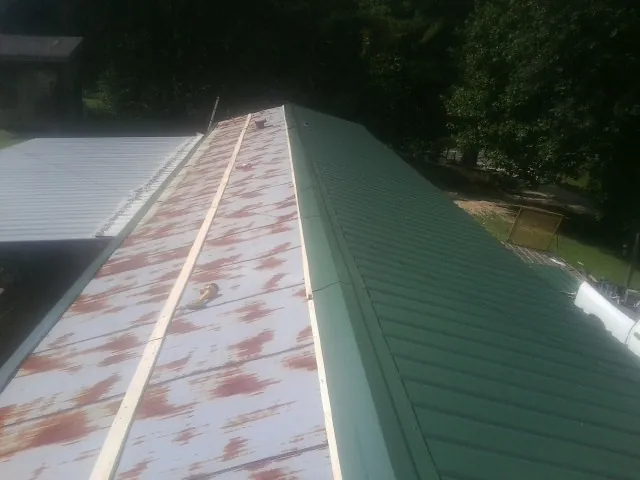 Old rusted panels beside newly installed green metal roofing — Wind Damage Roof Repair by Roofing Brothers in Cogan Station