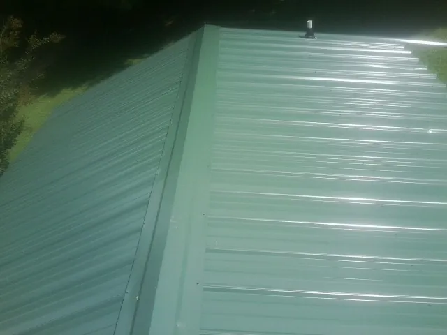 New green metal panels meeting at the ridge of a roof — Flat Roof Repair work by our crew in Cogan Station