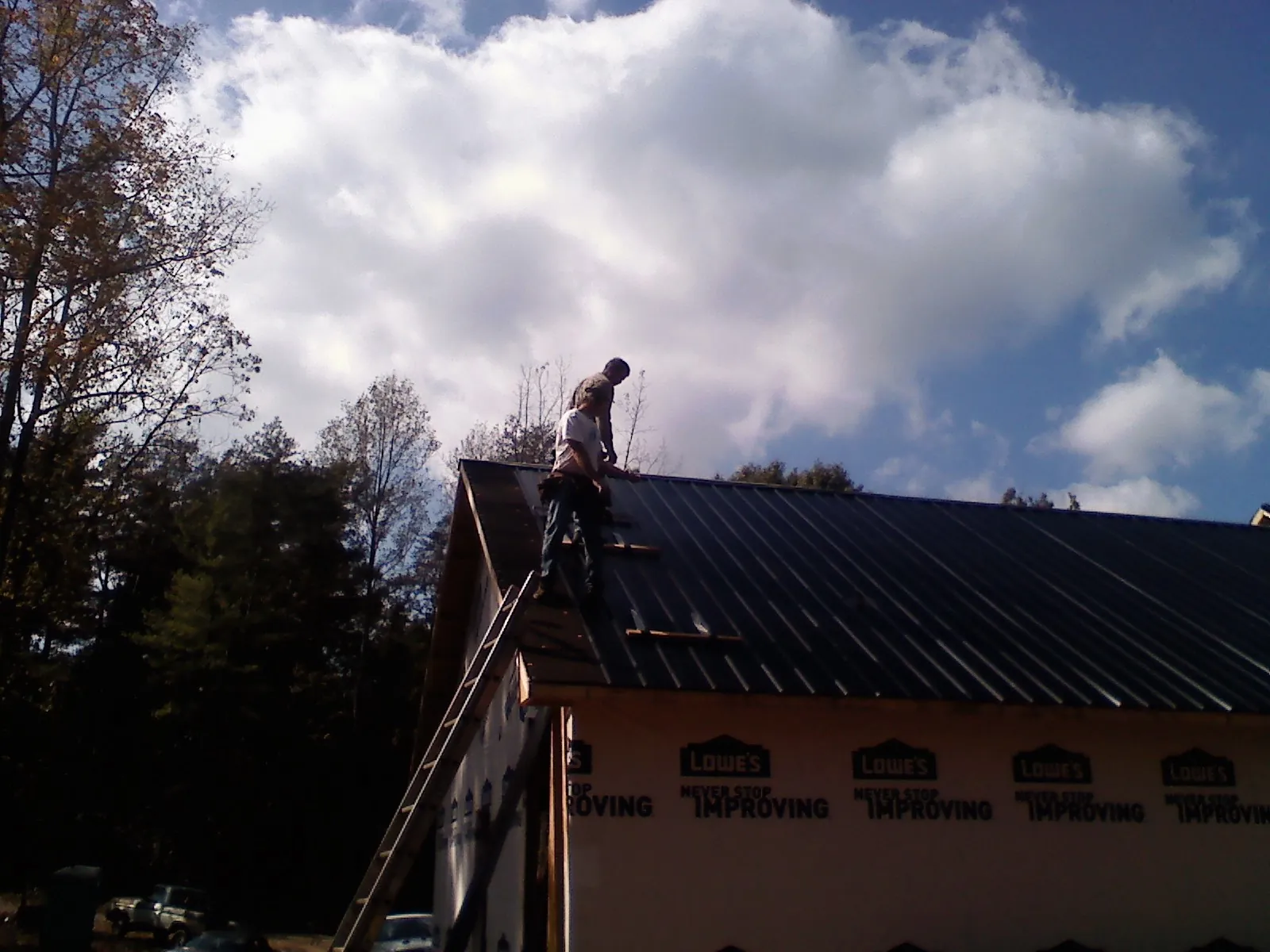Roofer fastening dark metal panels high against a cloudy sky, from a Roof Inspection job in Cogan Station