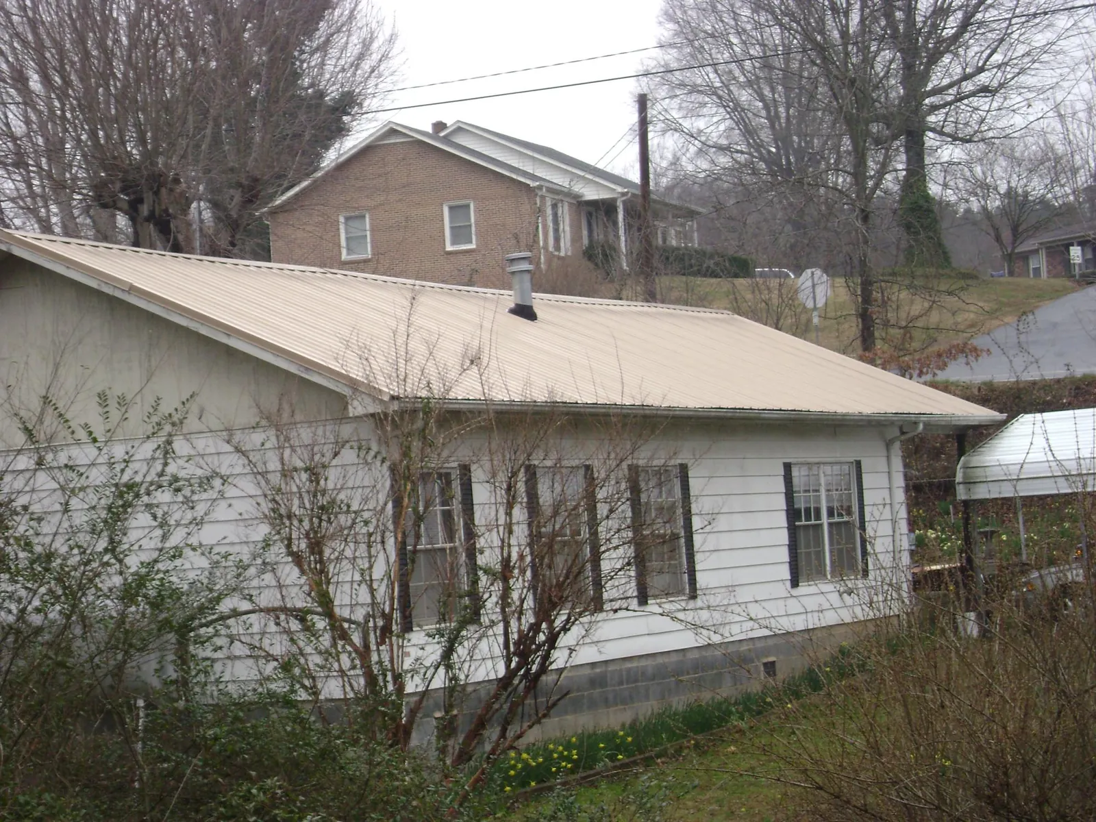 Tan metal roof on a white sided house set into a hillside — Commercial Roofing by Roofing Brothers in Cogan Station